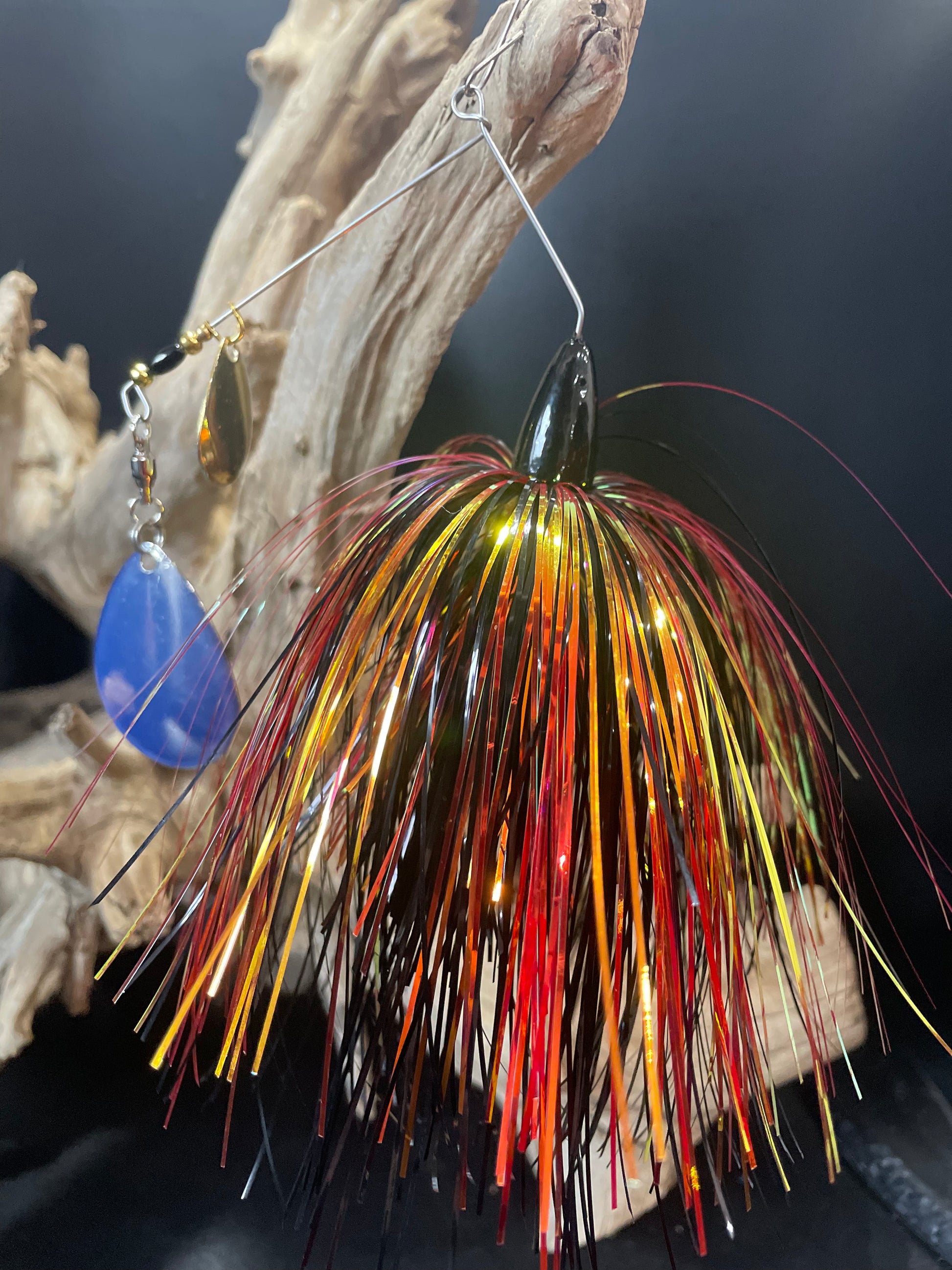 Introducing the Krakatoa, a bass spinnerbait fishing lure that combines black, gold, and red colours to attract fish and a #7 Colorado Blade with UV glow for added visibility. Available in 1/2 and 3/4 oz options with a #5/0 hook. Catch more bass with this ultimate fishing lure. Front facing picture