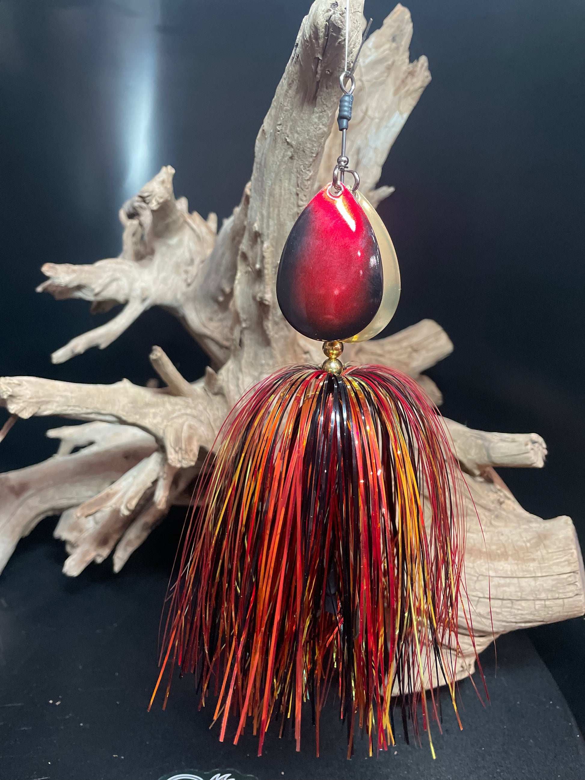 Fishing Bucktail lure that is black, gold and red. dual #8 blades, one gold and one black and red. pictured in front of driftwood.