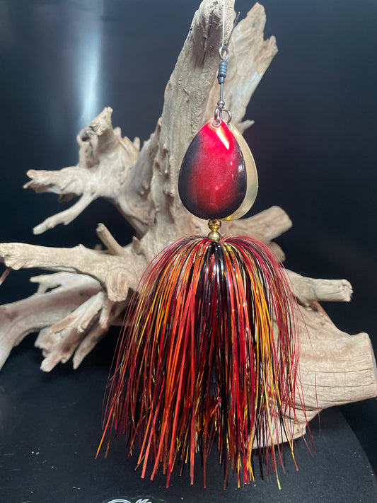 Fishing Bucktail lure that is black, gold and red. dual #8 blades, one gold and one black and red. pictured in front of driftwood.