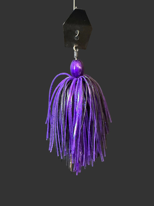 Purple and black Chatterbait fishing lure with a house-shaped top on a dark surface with driftwood. Lure-cifer